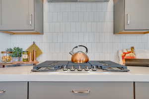 Kitchen view of gray cabinetry, backsplash, and stainless steel gas stovetop