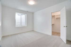 Unfurnished bedroom featuring light colored carpet and a walk in closet