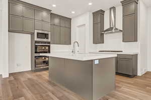 Kitchen featuring light wood-type flooring, gray cabinets, built in microwave, and wall chimney exhaust hood