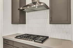 Kitchen with stainless steel gas stovetop, wall chimney range hood, and backsplash