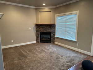 Unfurnished living room featuring a stone fireplace, carpet floors, and crown molding