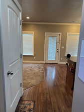 Doorway featuring dark wood-type flooring, a textured ceiling, and ornamental molding