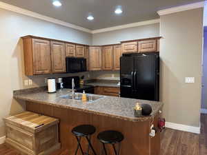 Kitchen with kitchen peninsula, dark hardwood / wood-style flooring, black appliances, and ornamental molding