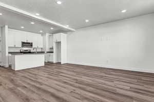 Kitchen with white cabinets, stainless steel appliances, hardwood / wood-style flooring, and an island with sink