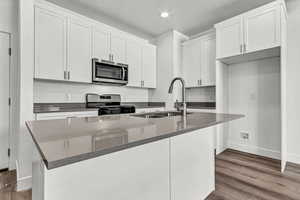 Kitchen with sink, stainless steel appliances, a center island with sink, white cabinets, and light wood-type flooring