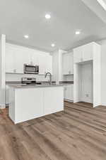 Kitchen with white cabinets, an island with sink, and light hardwood / wood-style floors