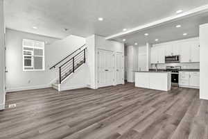 Kitchen featuring appliances with stainless steel finishes, a textured ceiling, a kitchen island with sink, hardwood / wood-style floors, and white cabinetry