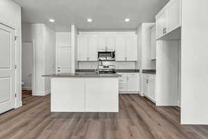 Kitchen with appliances with stainless steel finishes, white cabinetry, and a kitchen island with sink