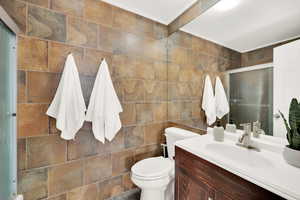 Bathroom featuring toilet, vanity, tile walls, and shower/tub combo.