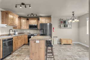 Kitchen featuring sink, an inviting chandelier, pendant lighting, a kitchen island, and black appliances