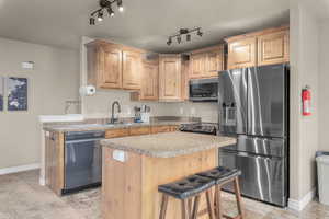 Kitchen with track lighting, a kitchen breakfast bar, sink, a kitchen island, and stainless steel appliances