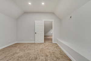 Bonus room with light colored carpet and vaulted ceiling