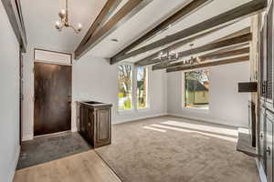 Foyer with vaulted ceiling with beams, wood-type flooring, and a notable chandelier