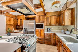 Kitchen with decorative backsplash, light wood-type flooring, premium range hood, stainless steel appliances, and sink