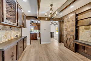 Hallway with a chandelier, beamed ceiling, and light hardwood / wood-style floors