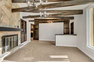 Unfurnished living room featuring light carpet, a fireplace, lofted ceiling with beams, and a notable chandelier