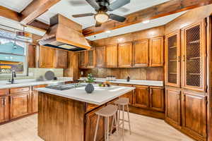 Kitchen with a kitchen island, sink, light wood-type flooring, and premium range hood