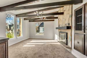 Unfurnished living room featuring a chandelier, a stone fireplace, a wealth of natural light, and light colored carpet