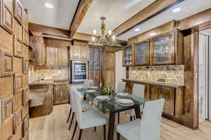 Dining area with a chandelier, beam ceiling, beverage cooler, and light hardwood / wood-style flooring