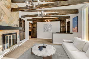 Living room featuring a notable chandelier, lofted ceiling with beams, and a stone fireplace