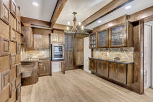 Kitchen featuring beverage cooler, hanging light fixtures, tasteful backsplash, beamed ceiling, and light wood-type flooring