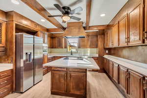 Kitchen with beamed ceiling, appliances with stainless steel finishes, light wood-type flooring, and a kitchen island