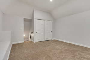 Unfurnished bedroom featuring light carpet, a closet, and lofted ceiling