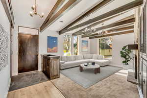 Living room with vaulted ceiling with beams, dark hardwood / wood-style flooring, and a chandelier