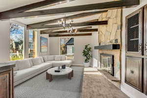 Carpeted living room featuring lofted ceiling with beams, a stone fireplace, and a chandelier