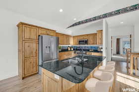 Kitchen featuring appliances with stainless steel finishes, vaulted ceiling, dark stone counters, and sink