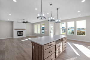 Kitchen featuring a large fireplace, light hardwood / wood-style floors, decorative light fixtures, a kitchen island, and ceiling fan with notable chandelier