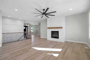 Unfurnished living room with a fireplace, light hardwood / wood-style flooring, and ceiling fan with notable chandelier