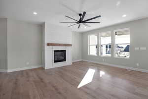 Unfurnished living room featuring ceiling fan, a large fireplace, and light wood-type flooring