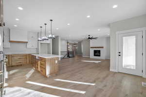 Kitchen featuring a large fireplace, white cabinets, light hardwood / wood-style floors, a kitchen island, and hanging light fixtures