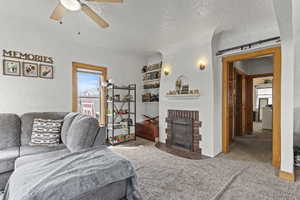 Carpeted living room with a ceiling fan, a textured wall, a textured ceiling, and a fireplace