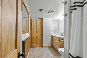 Bathroom with tile patterned floors, vanity, toilet, and a textured ceiling