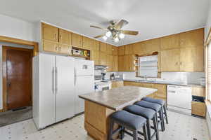 Kitchen with white appliances, ceiling fan, sink, a center island, and a breakfast bar area