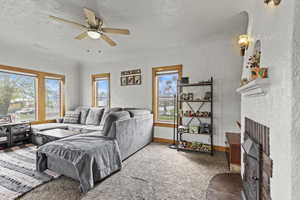 Living room featuring a textured ceiling, ceiling fan, a textured wall, a fireplace, and visible vents