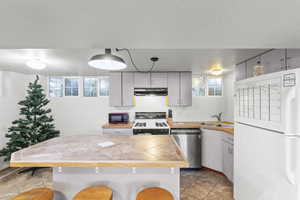 Kitchen featuring sink, a kitchen breakfast bar, tile countertops, pendant lighting, and white appliances