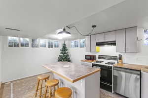 Kitchen with a center island, stainless steel dishwasher, decorative light fixtures, a breakfast bar area, and white range with gas cooktop