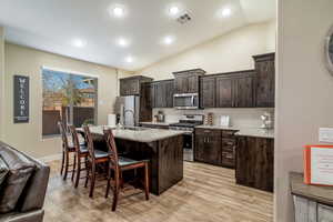 Kitchen with a kitchen breakfast bar, lofted ceiling, an island with sink, and appliances with stainless steel finishes