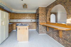 Kitchen featuring a center island, oven, light wood-type flooring, white fridge with ice dispenser, and brick wall
