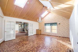 Unfurnished living room with built in shelves, lofted ceiling, ceiling fan with notable chandelier, and french doors