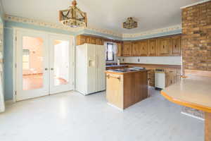 Kitchen with french doors, decorative light fixtures, white refrigerator with ice dispenser, and light hardwood / wood-style flooring