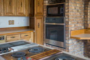 Kitchen featuring backsplash, stainless steel appliances, and brick wall