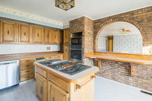 Kitchen featuring ceiling fan, a center island, stainless steel appliances, and brick wall