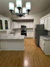 Kitchen featuring kitchen peninsula, appliances with stainless steel finishes, sink, decorative light fixtures, and light hardwood / wood-style floors