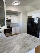 Kitchen with white cabinetry, stainless steel appliances, vaulted ceiling, and light wood-type flooring