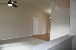 Carpeted spare room with ceiling fan and vaulted ceiling