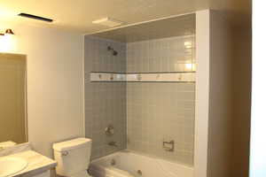 Full bathroom with tiled shower / bath combo, toilet, a textured ceiling, and vanity